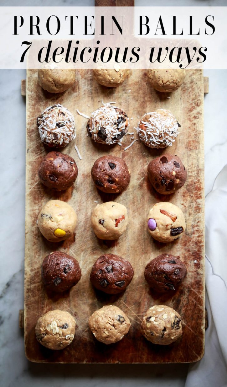 Photo of six different flavors of peanut butter protein balls on a cutting board, including: oatmeal raisin, double chocolate, trail mix, mocha, almond joy, and peanut butter oatmeal. 