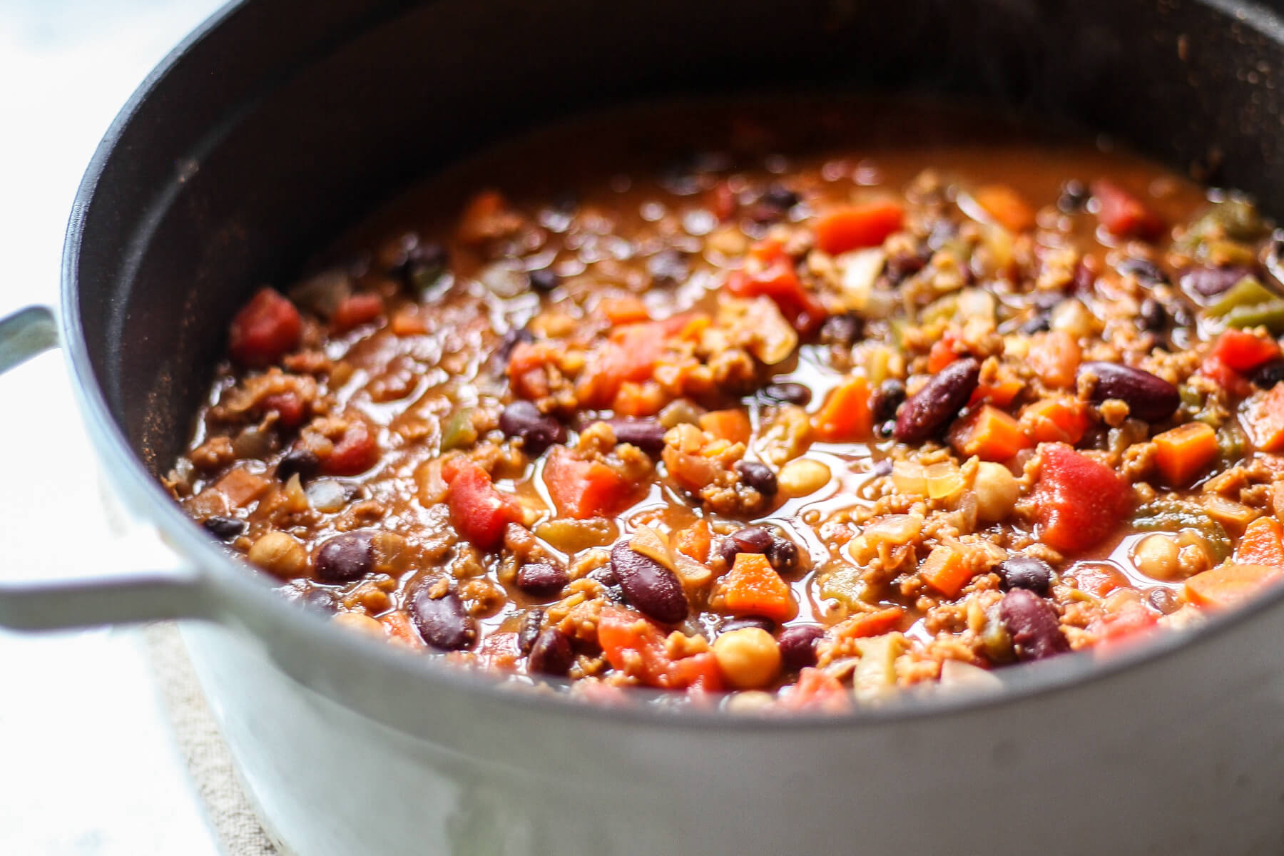 A close up photograph of vegan chili with chickpeas and beans that's finished simmering in a pot.