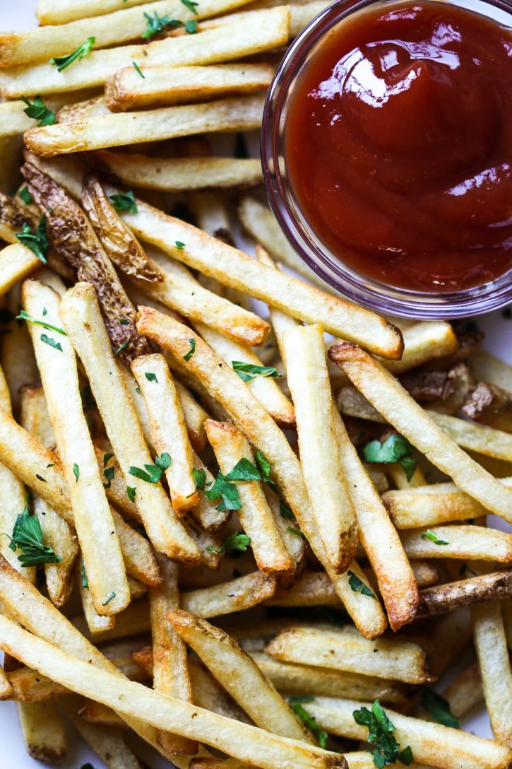A close up photograph of perfectly cooked golden french fries garnished with parsley. 