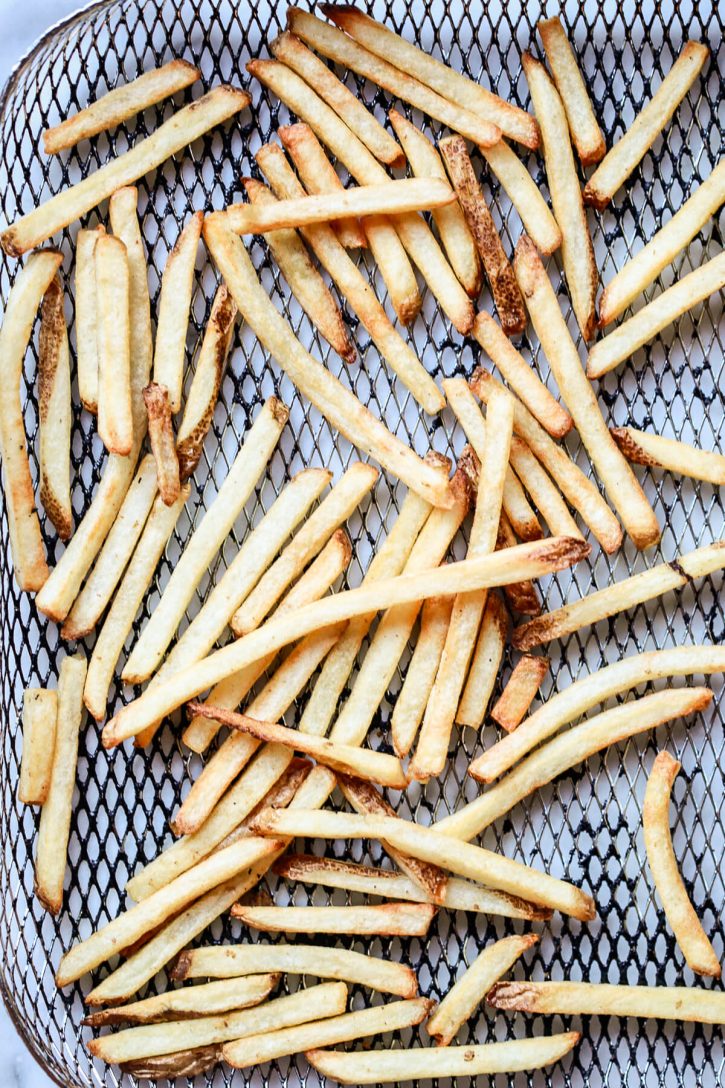 Air fryed frozen french fries are seen in an air fryer basket on a kitchen counter. 