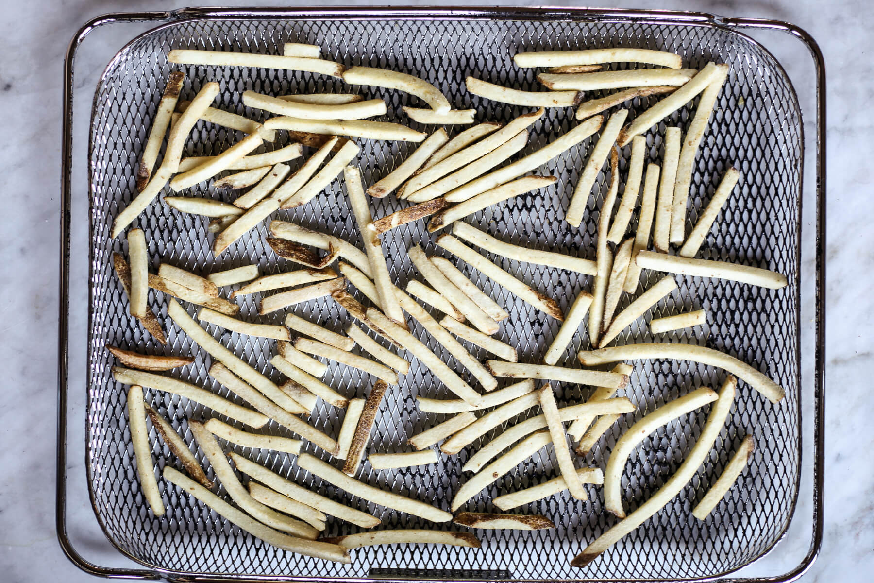 An overhead photograph of frozen French fries arranged in a air fryer basket.
