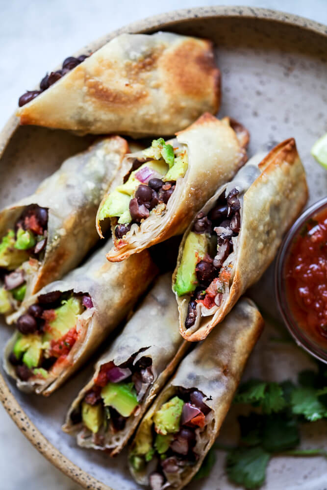 A plate of crispy avocado and black bean egg rolls with salsa on the side. 