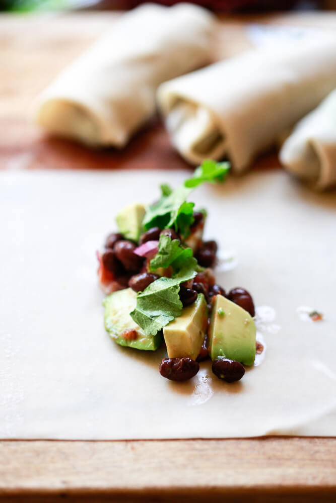 Avocado, black beans, cilantro, and salsa on an egg roll wrapper before getting wrapped. 