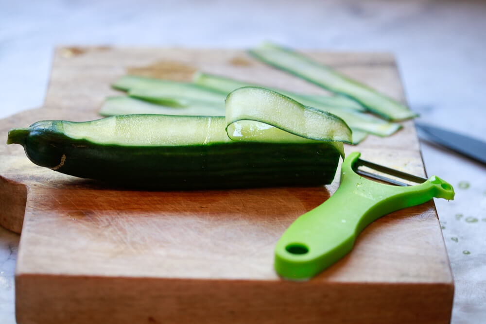 An English cucumber is cut into ribbons with a vegetable peeler.