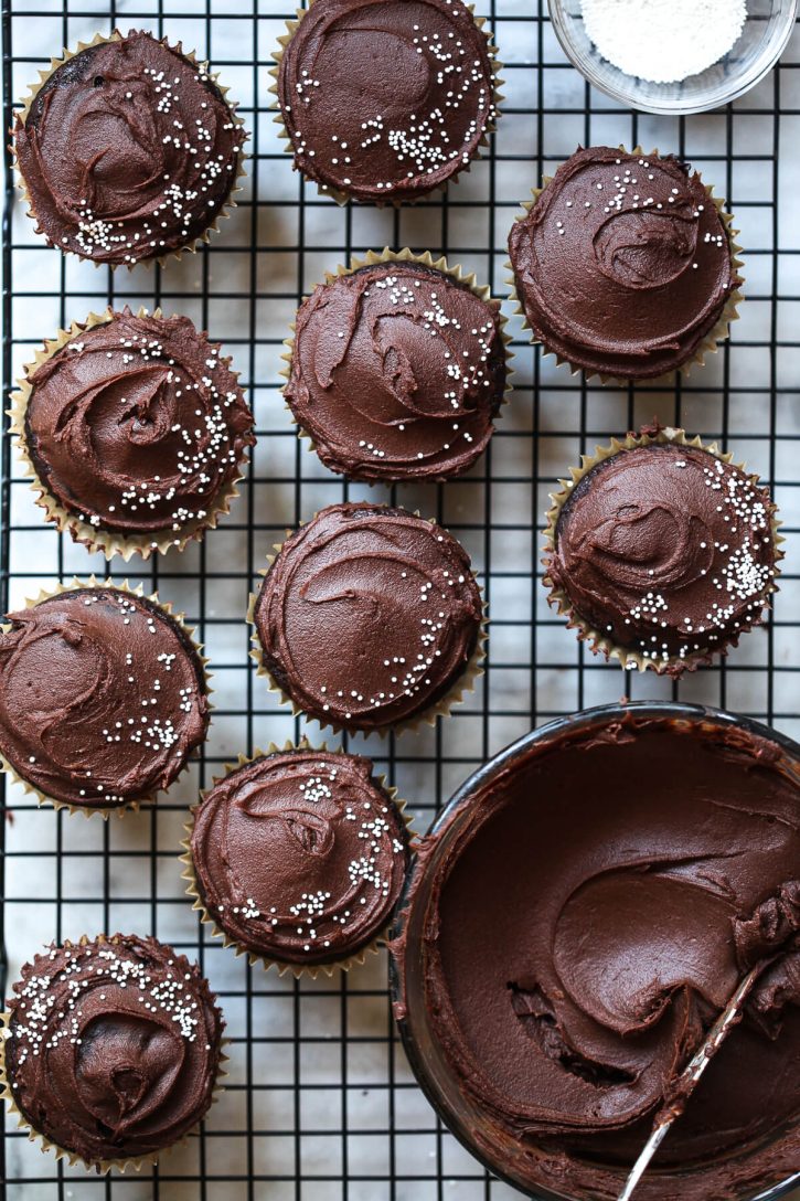 Vegan chocolate cupcakes on a cooling wrack with chocolate frosting and sprinkles. 