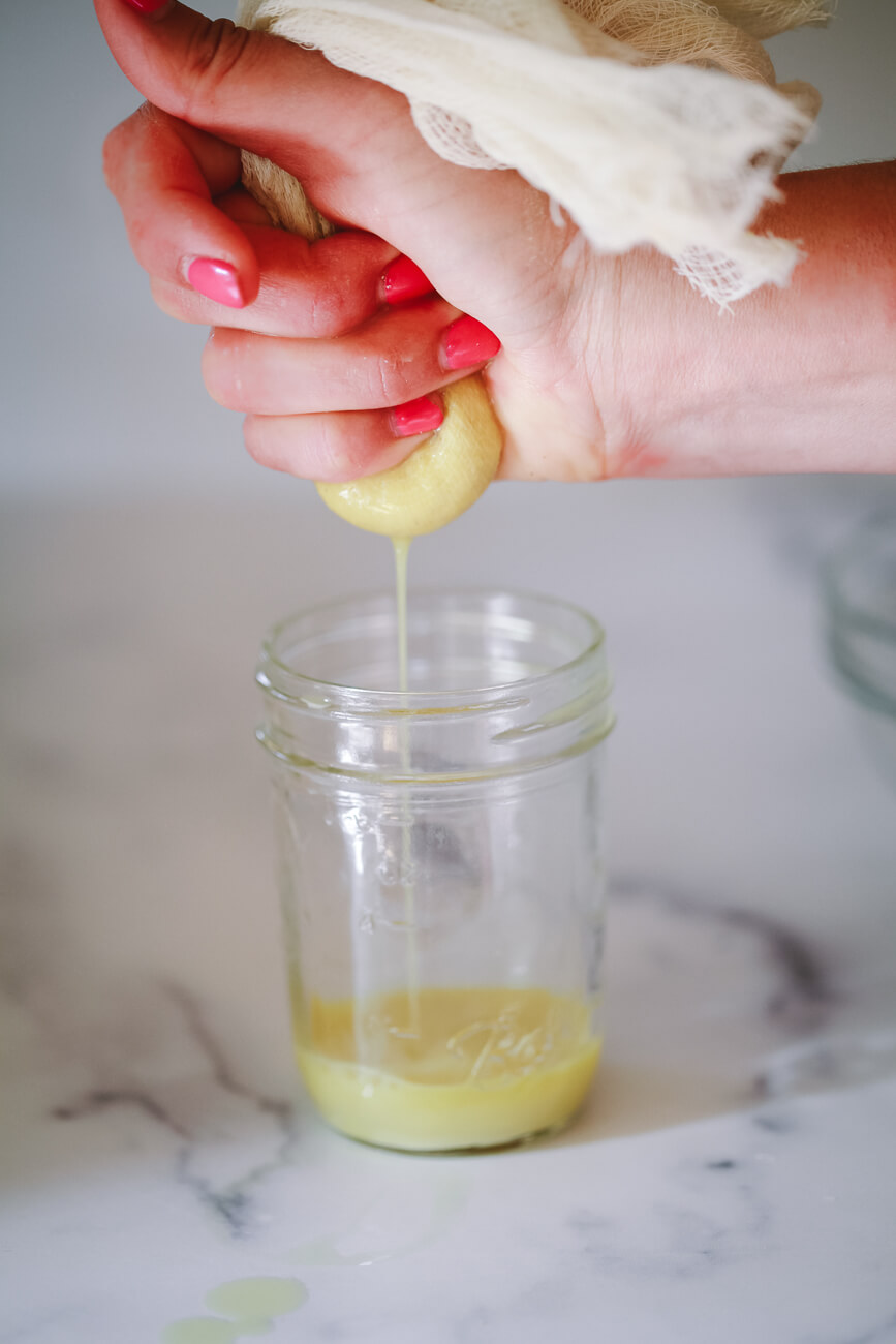 Cheesecloth filled with freshly grated ginger is squeezed over a small jar to make ginger juice.