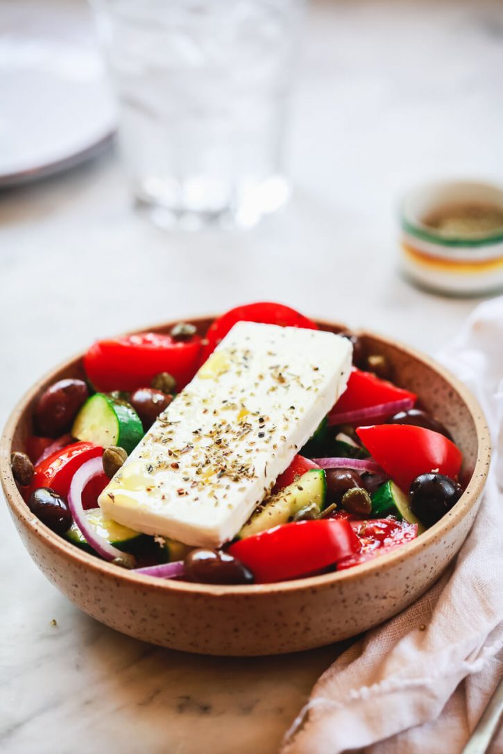 A photograph of a bowl filled with traditional Greek village salad made with tomatoes, cucumber, olives, onion, and topped with feta cheese. 