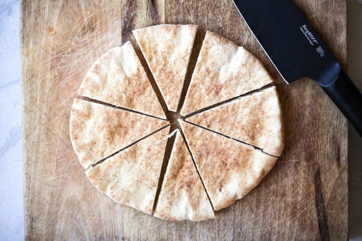 A piece of round pita bread is cut into eight pieces on a cutting board. 