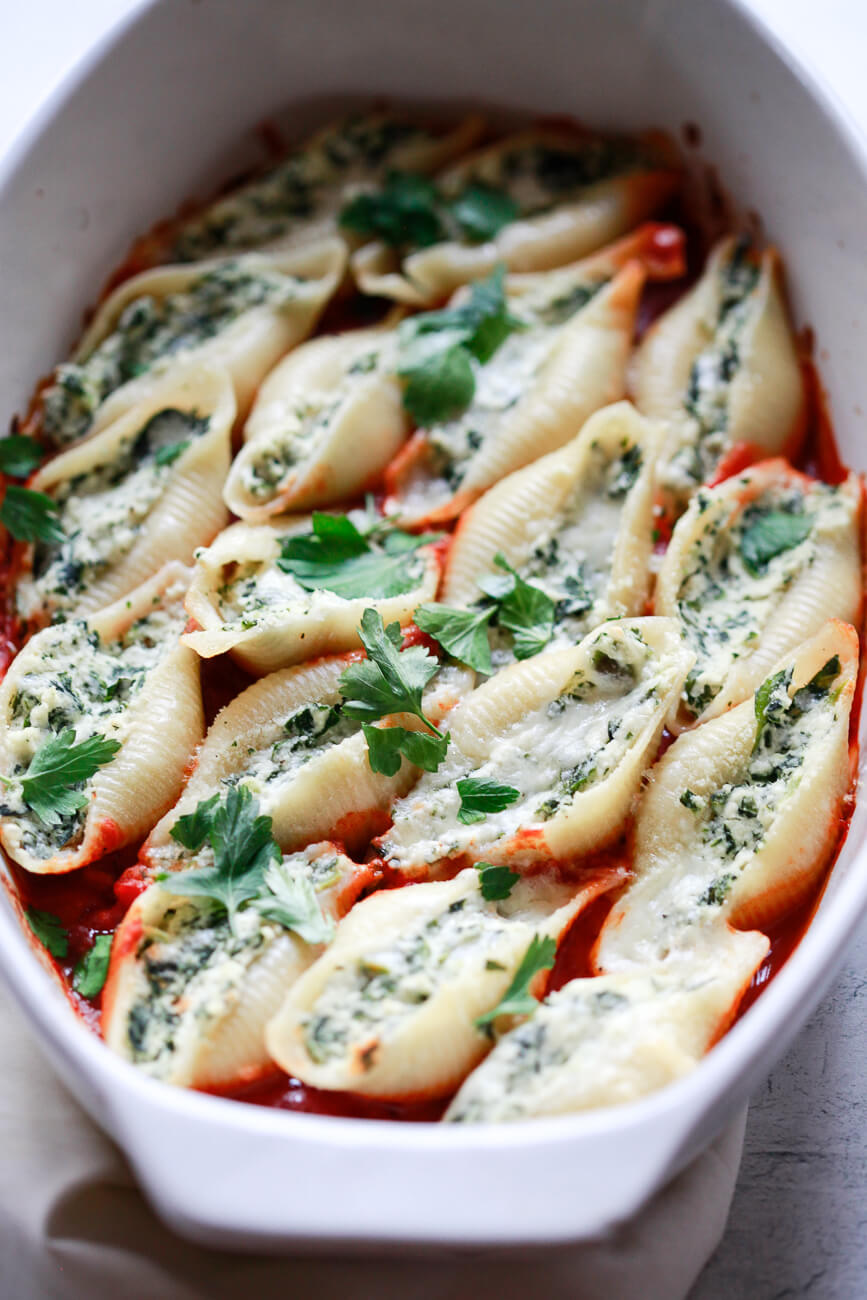 A white casserole dish filled with baked ricotta stuffed shells (Conchiglioni) on top of red sauce and garnished with parsley. This vegan stuffed shells recipe is just like the classic version. 