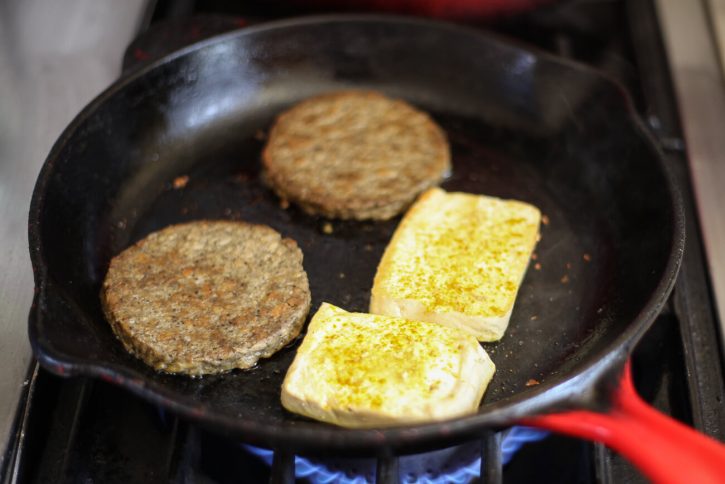 Vegan breakfast sausage patties and slices of high protein tofu cook in a cast iron skillet on the stove to make an easy high protein vegan breakfast.