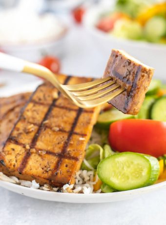 A bowl of veggies and rice topped with grilled tofu.