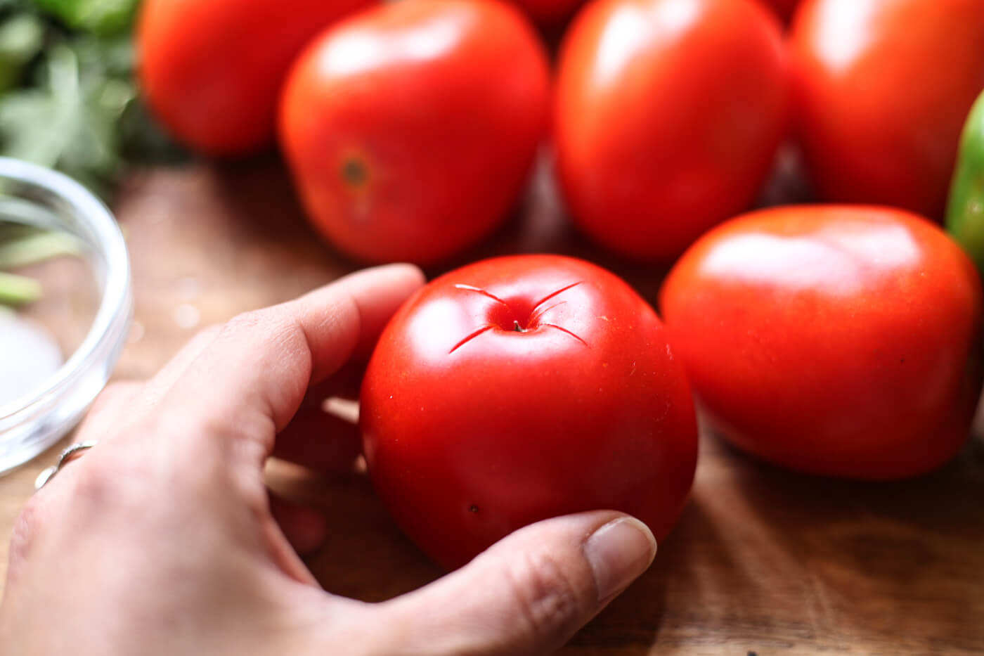 An x is cut into the bottom of a red tomato.