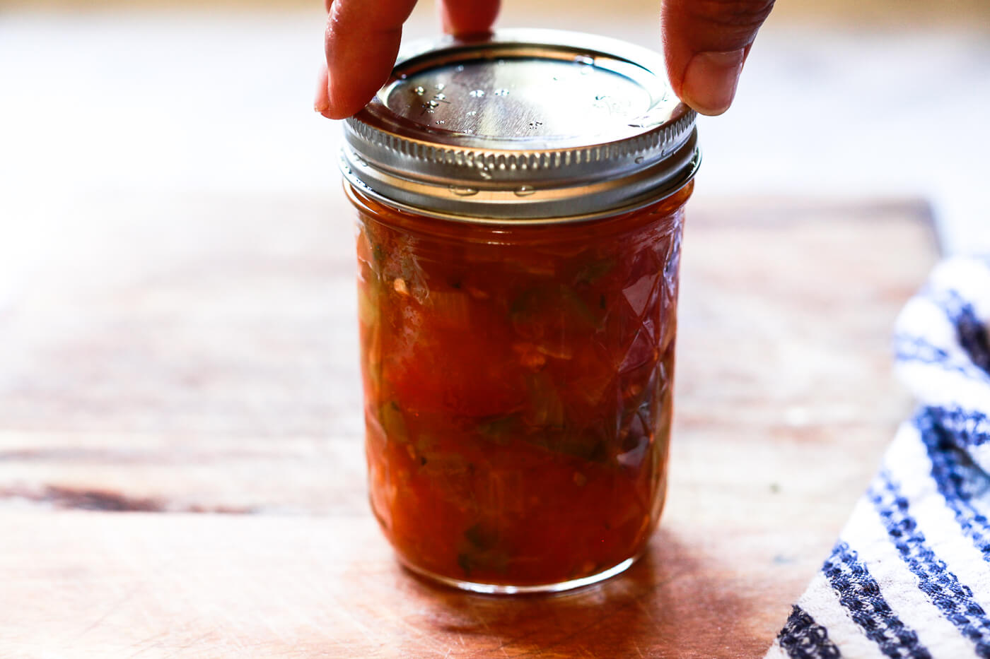 A Ball canning lid is placed on a jar of homemade salsa for canning.
