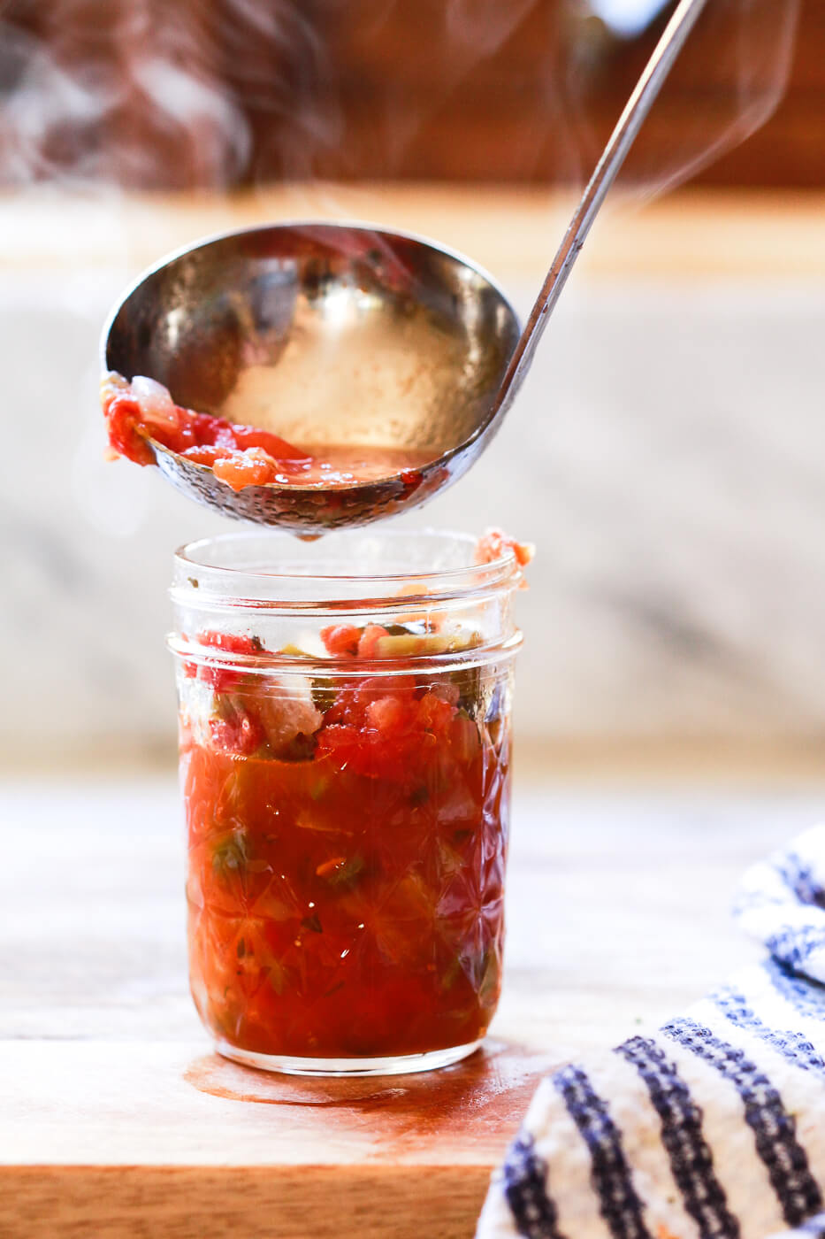Hot steaming homemade salsa is ladled into a hot Ball mason jar. 