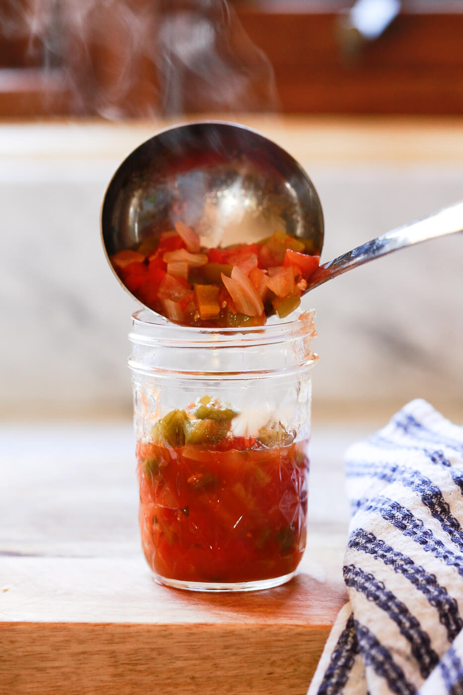 Hot canning salsa is ladled into a warm Ball canning jar.