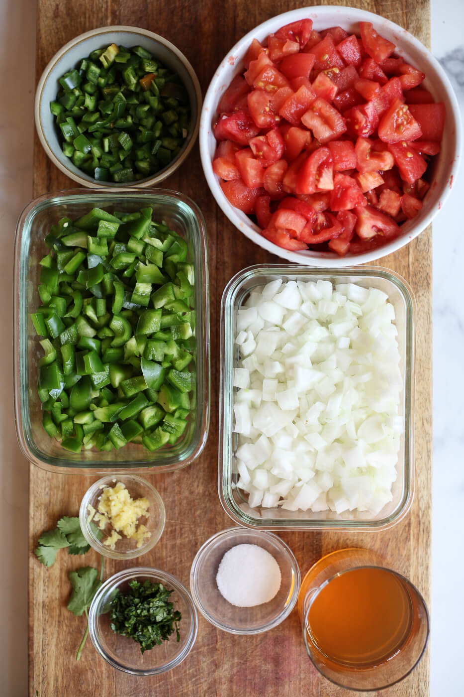 The ingredients for homemade canned salsa are prepared on a cutting board and include tomatoes, bell pepper, onion, jalapeno, garlic, cilantro, salt, and apple cider vinegar. 
