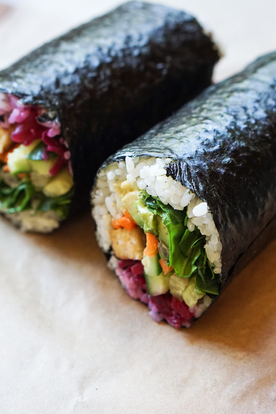 A close up photo of a vegan sushi burrito filled with spinach, avocado, cucumber, carrots and tempeh. 