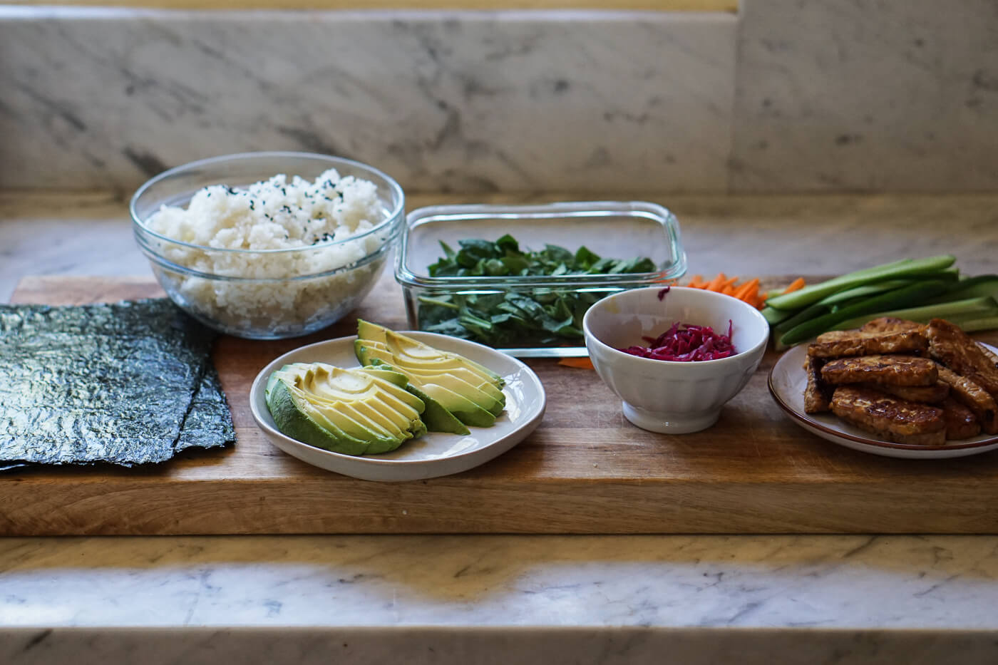 The ingredients for sushi burritos set on a cutting board.