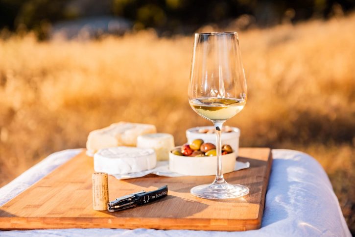 A beautiful outdoor picnic with white wine, cheese, and olives. 