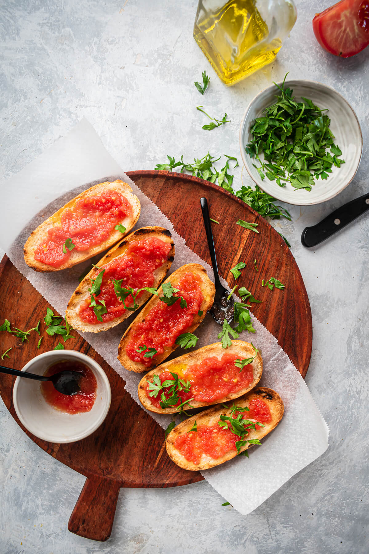 A beautiful overhead photo of 5 pieces of pan con tomate on a wood cutting board on a light grey background.