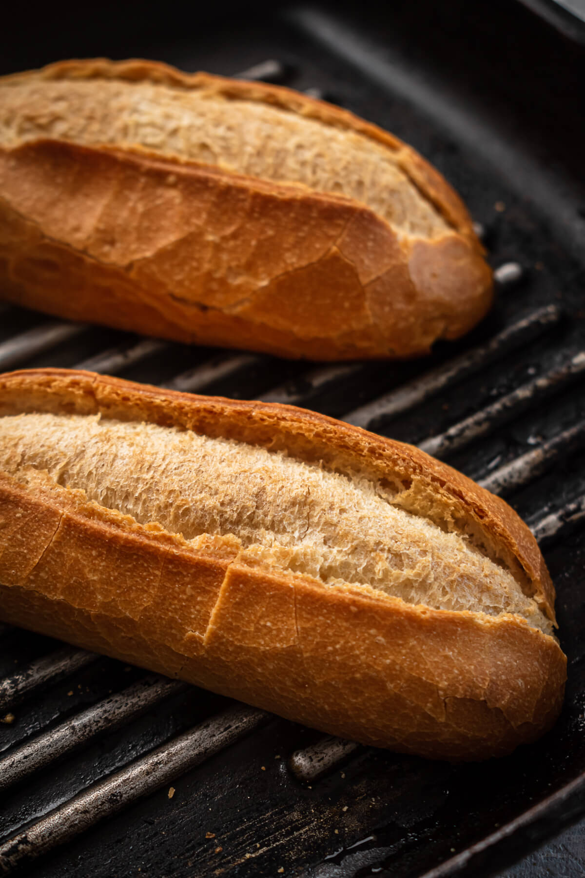 Baguette halves toast on a grill.