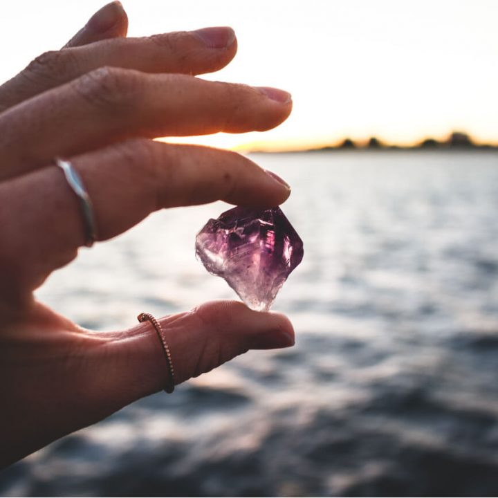 A woman's hand holds an amethyst crystal in front of the ocean.