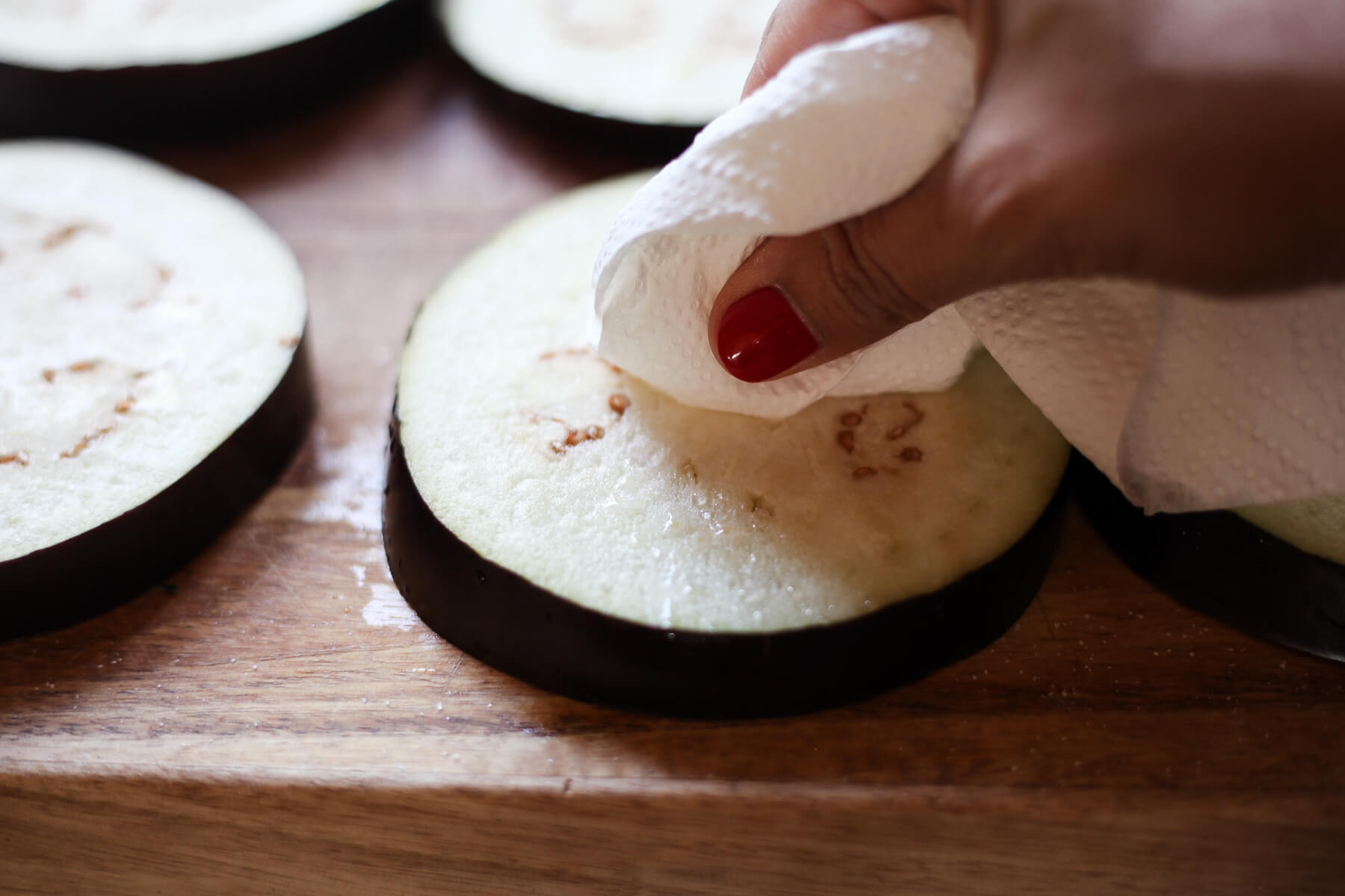 Water and salt is wiped off of a salted eggplant round with a paper towel.