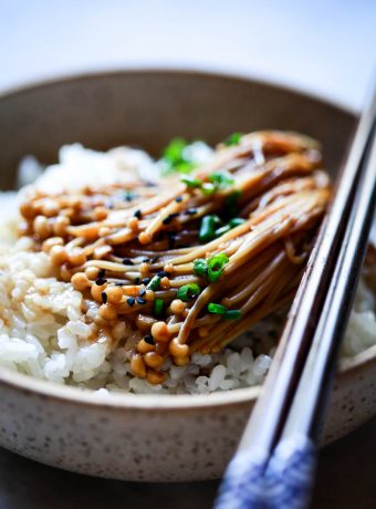 Enoki mushrooms with teriyaki and soy sauce served over rice and topped with chives and black sesame seeds.