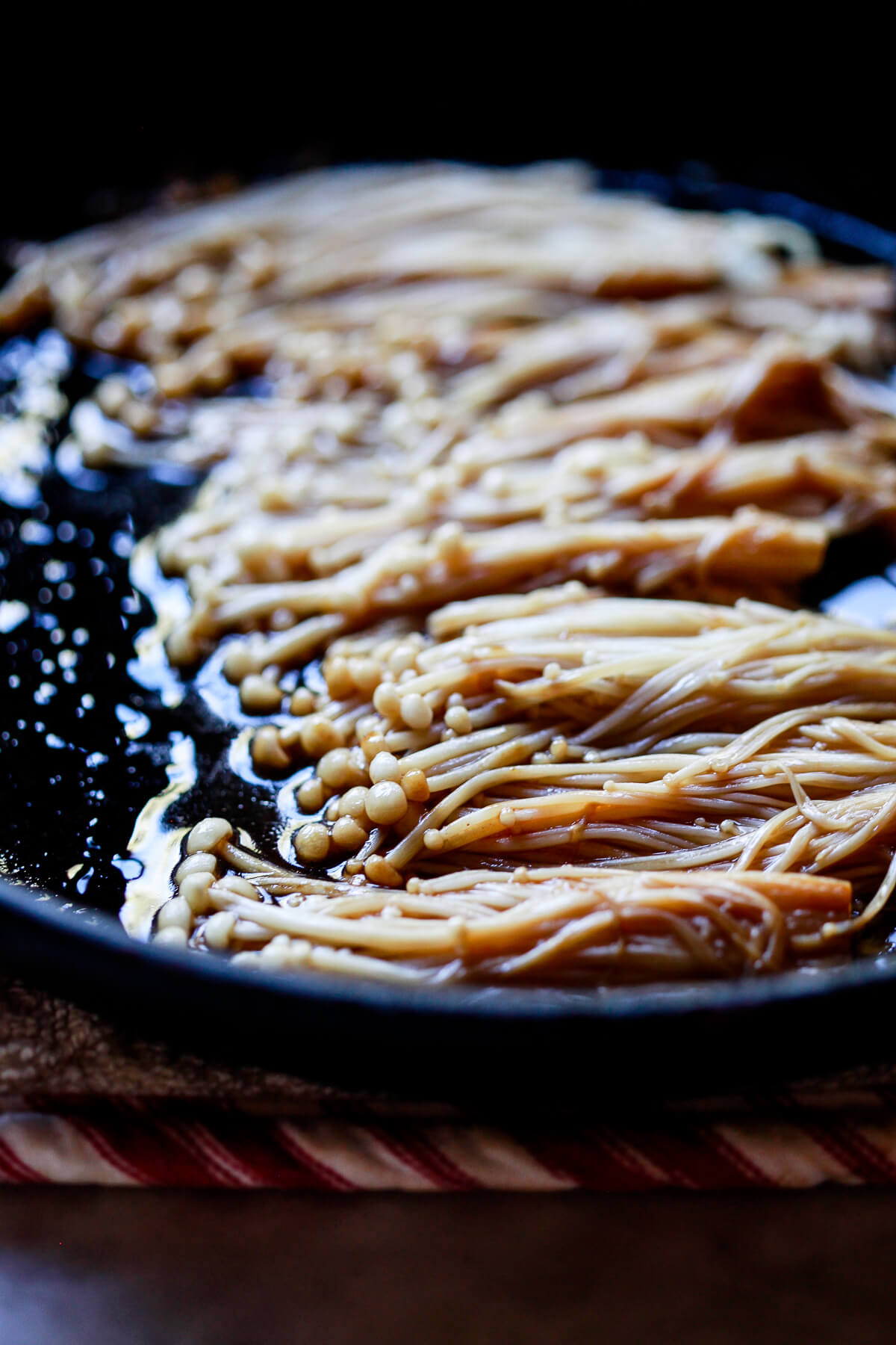Enoki mushrooms cook in soy sauce and teriyaki sauce in a cast iron skillet.