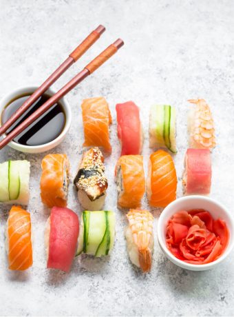 An overhead photo of a variety of nigiri including salmon, ahi, and cucumber over rice. A bowl of soy sauce sits at the left corner.