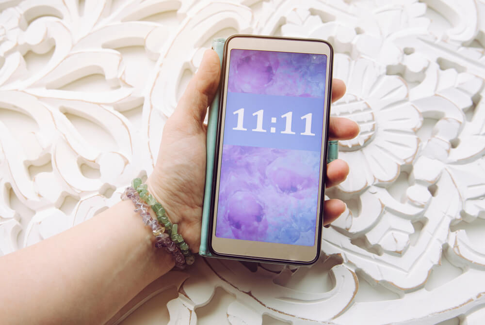 A hand holds a phone with 11:11 on the screen to show an angel number. 
