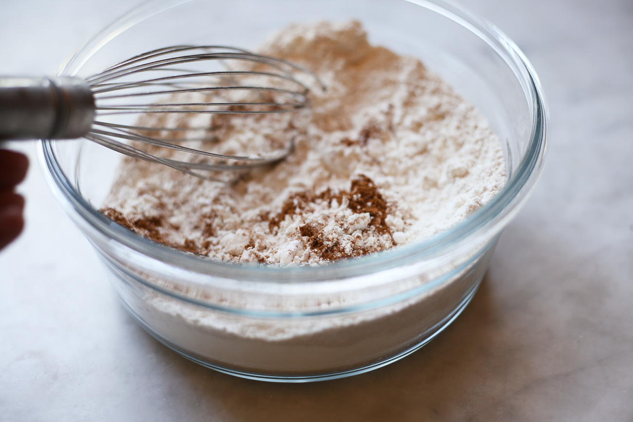 Flour, baking soda, and cinnamon are whisked together in a glass bowl.