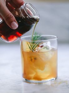 A small jar of homemade Demerara syrup is poured into an old fashioned bourbon cocktail.