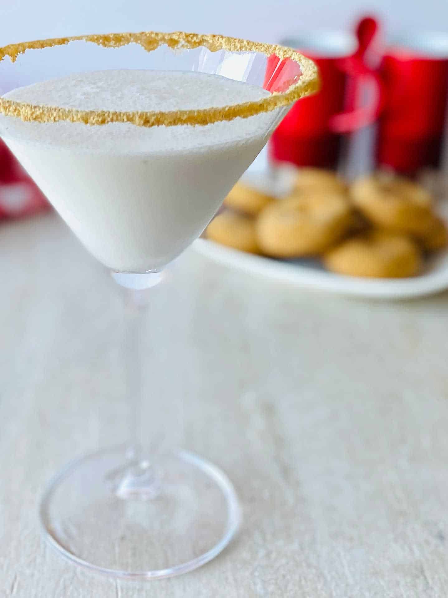 A martini glass with a gold sugar rim filled with a white creamy gingerbread martini Christmas cocktail. 