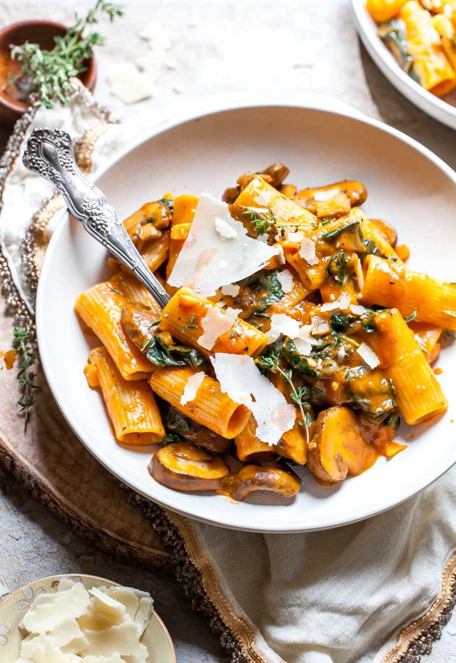 A white bowl filled with pumpkin pasta alla vodka with mushrooms and spinach. 