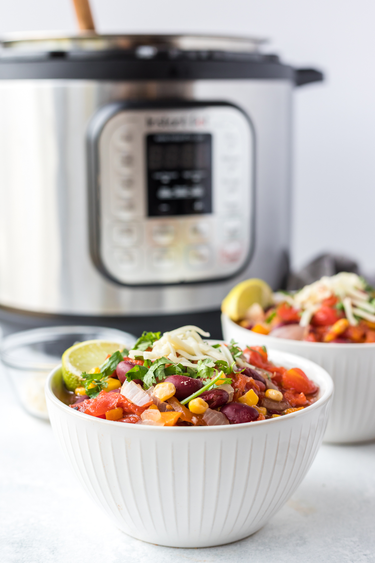 A white bowl filled with vegetarian taco soup garnished with cilantro and cheese sits in front of an Instant Pot in a white kitchen. 