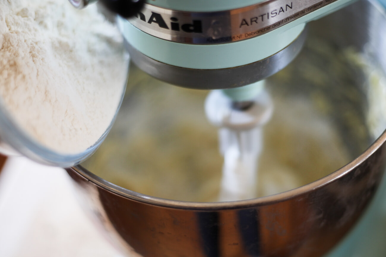 Flour is added to butter and sugar in a mixer.