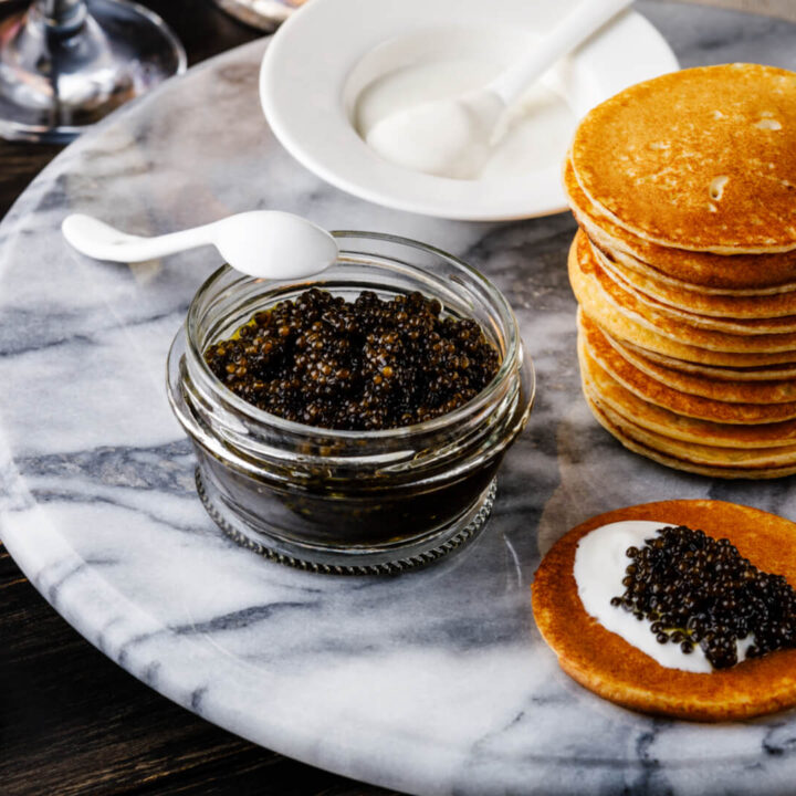 A small dish of caviar next to a stack of Russian blini pancakes.