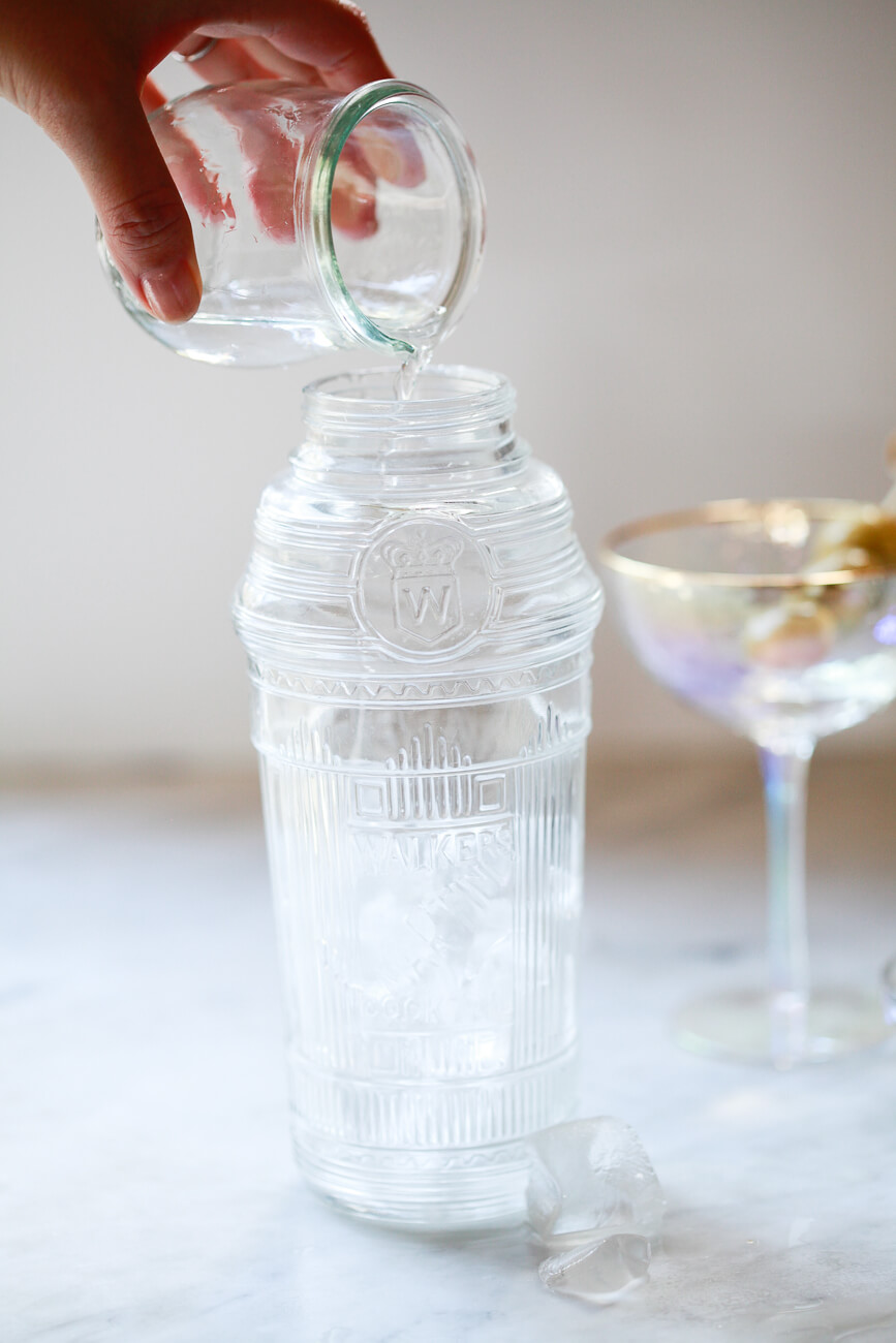 A small glass filled with 2.5 ounces of gin or vodka is poured into a vintage crystal cocktail shaker filled with ice.
