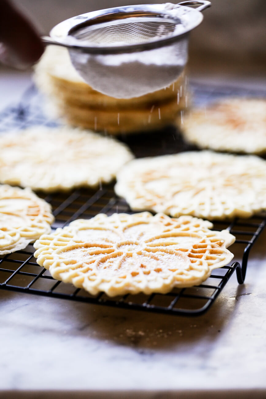 Powdered sugar is sifted over homemade pizzelle cookies on a cooling rack. 