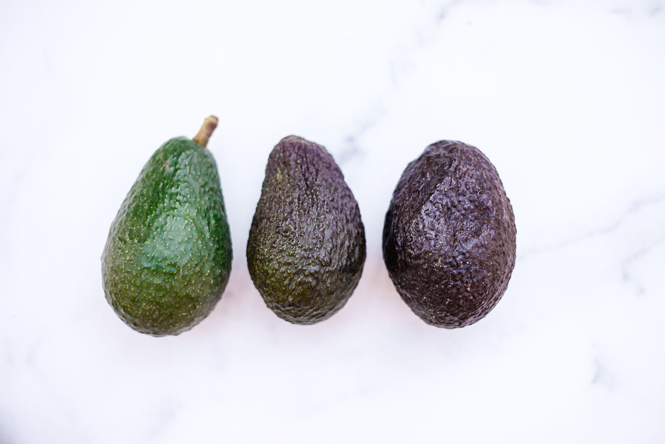 Three avocados of varying ripeness on a white marble background. 