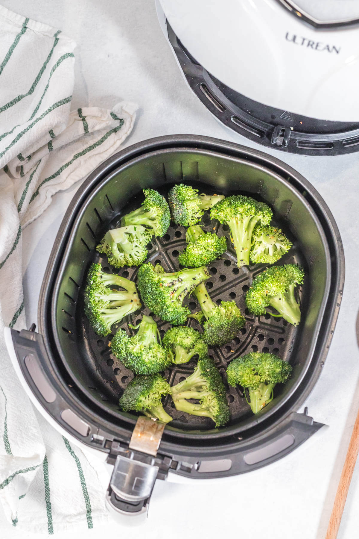 Seasoned broccoli florets in the basket of a white air fryer. 