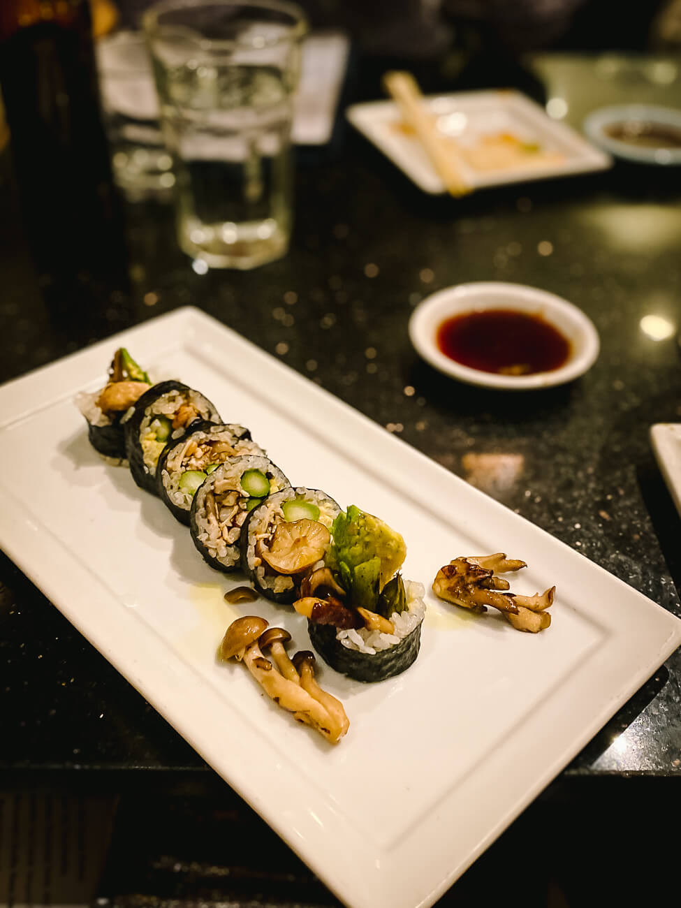 A white plate with a vegan mushroom sushi roll in a restaurant. 