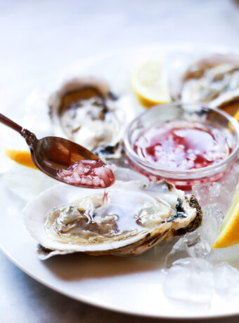 A small spoon of shallot mignonette sauce is spooned over a raw oyster on the half shell.