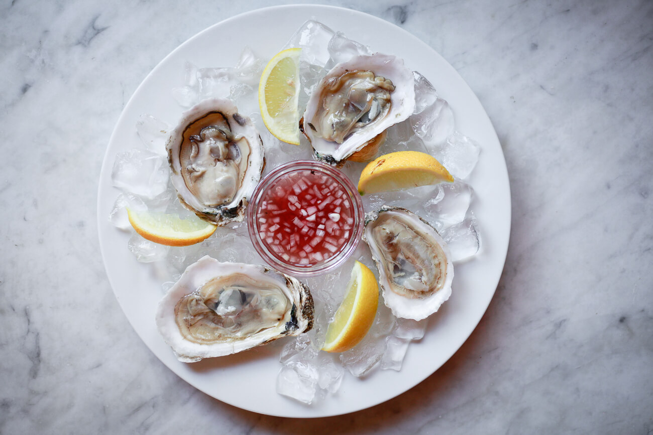 Four raw oysters on the half shell with a small bowl of mignonette sauce in the middle.