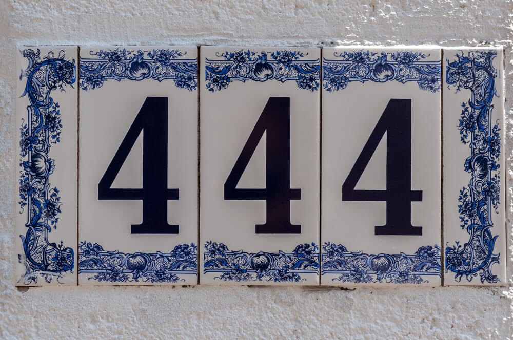 White and blue ceramic address tiles on a white wall. The number 444 in black. 