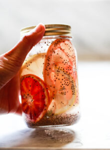 A mason jar filled with chia seeds in water with citrus slices gets picked up from a marble countertop.