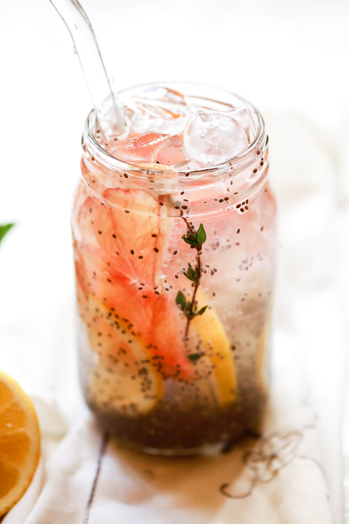A mason jar filled with a chia drink made out of chia seeds in water with citrus slices and a sprig of thyme. 
