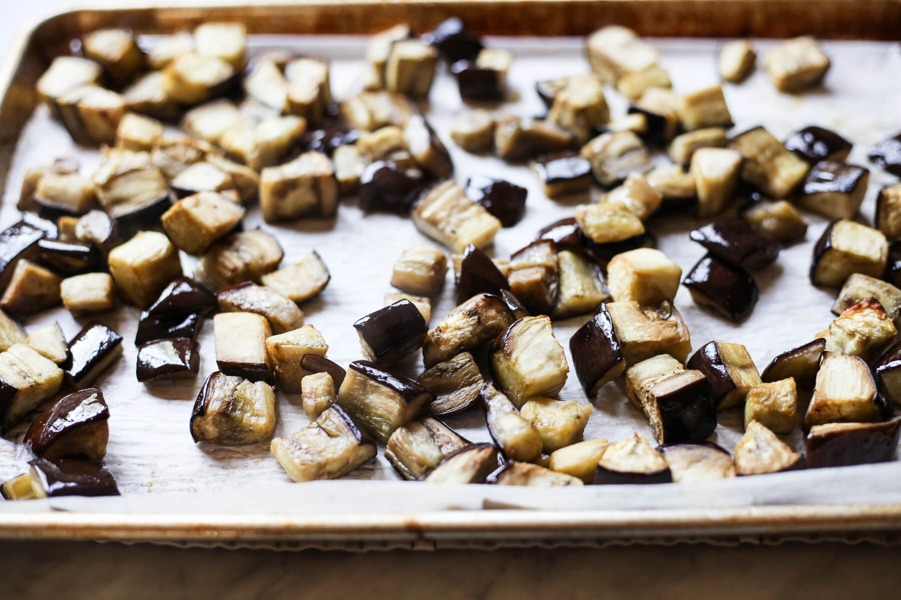 Roasted eggplant cubes on a parchment-lined baking sheet.