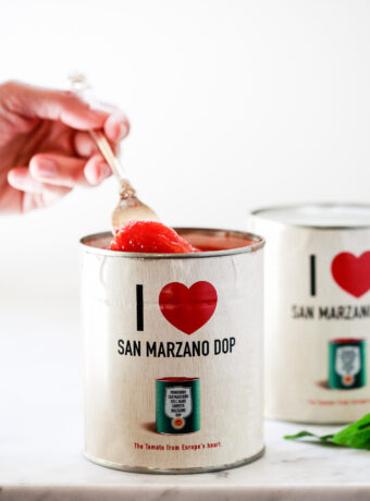 A fork lifts a single tomato out of a can of I heart san marzano dop cans.